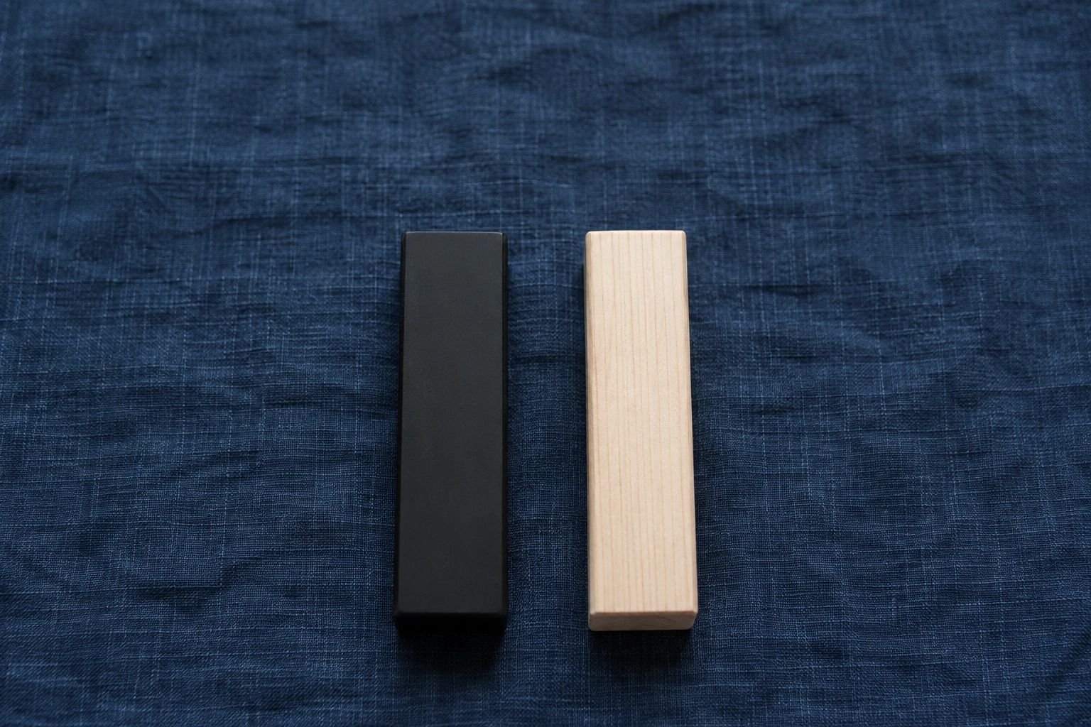 A black resin block and a pale wooden block of the same size laid side by side on indigo linen