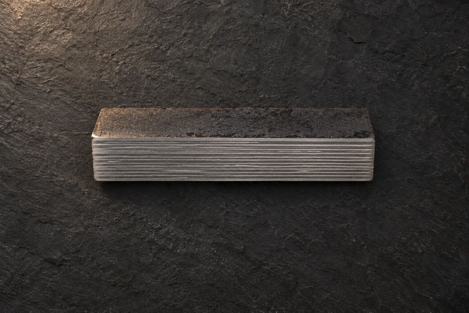 A steel bar on dark slate whose side shows thin, straight parallel layers