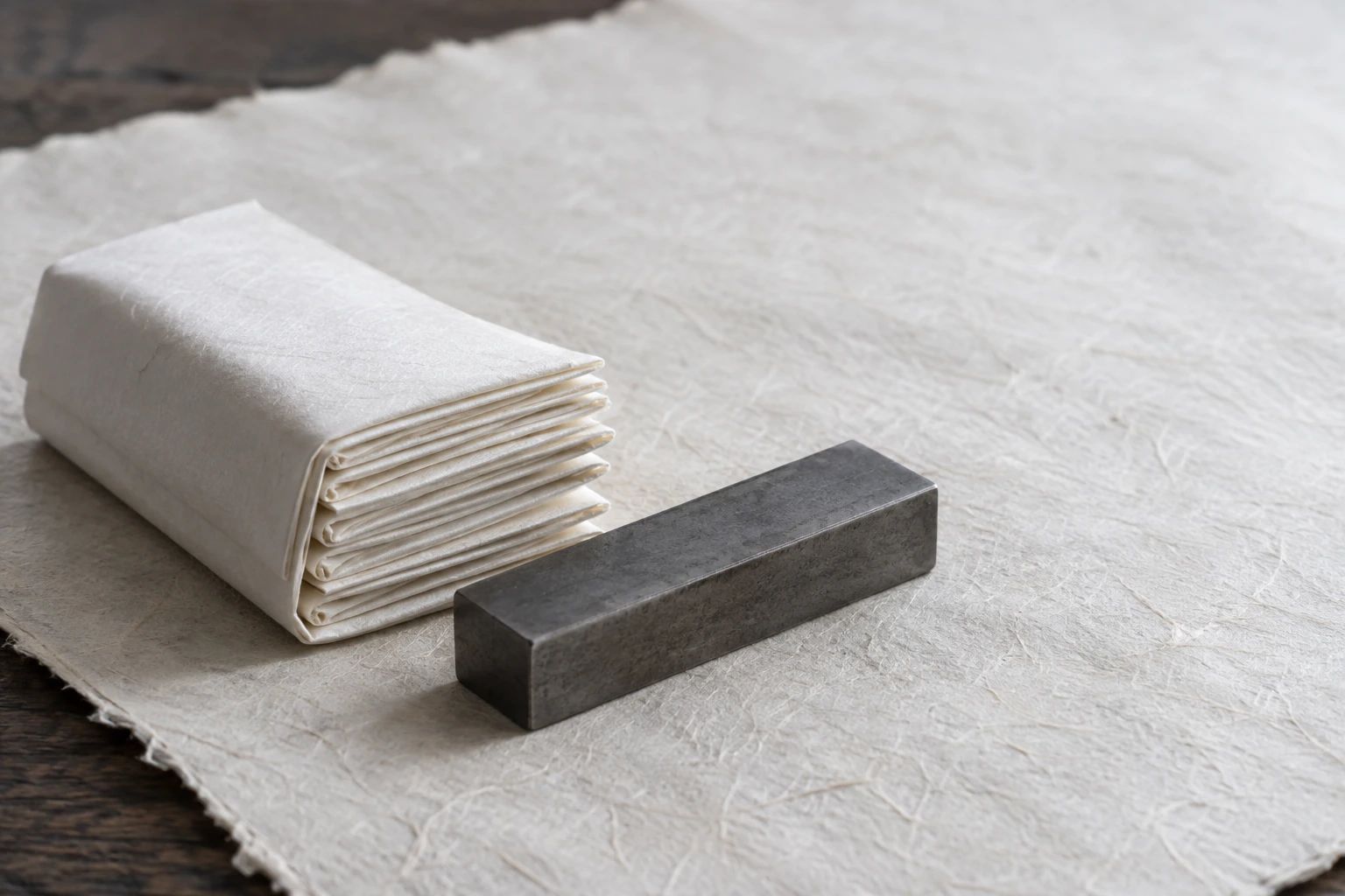 A bundle of many-times-folded washi paper beside a plain forged steel bar