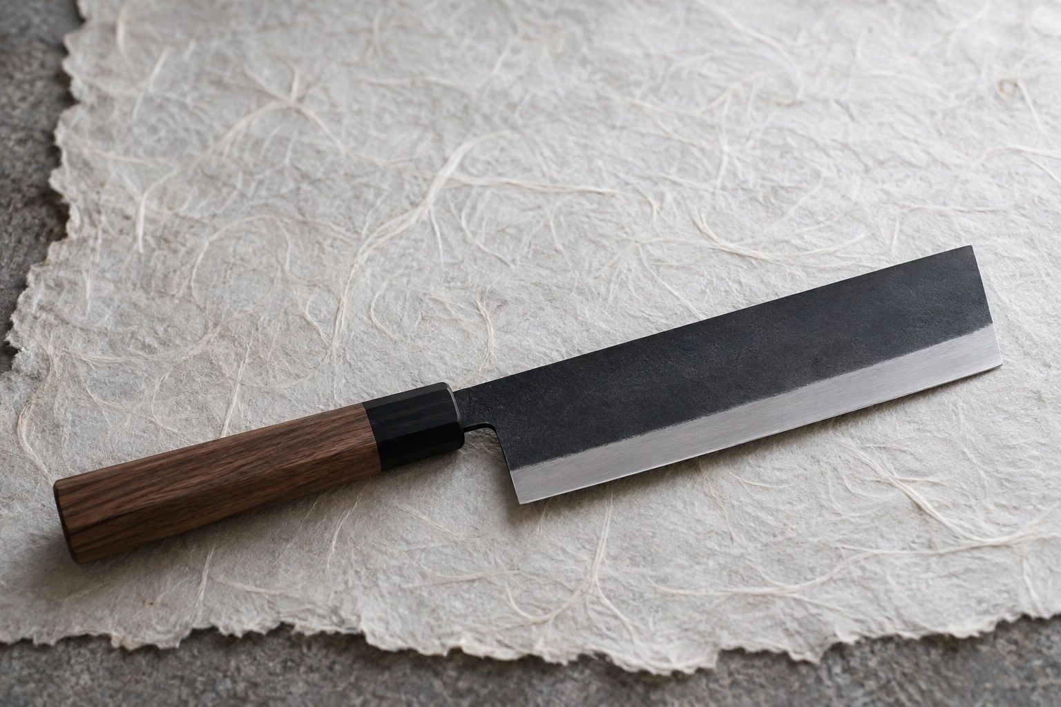 A nakiri with a black kurouchi finish lying diagonally on handmade white washi