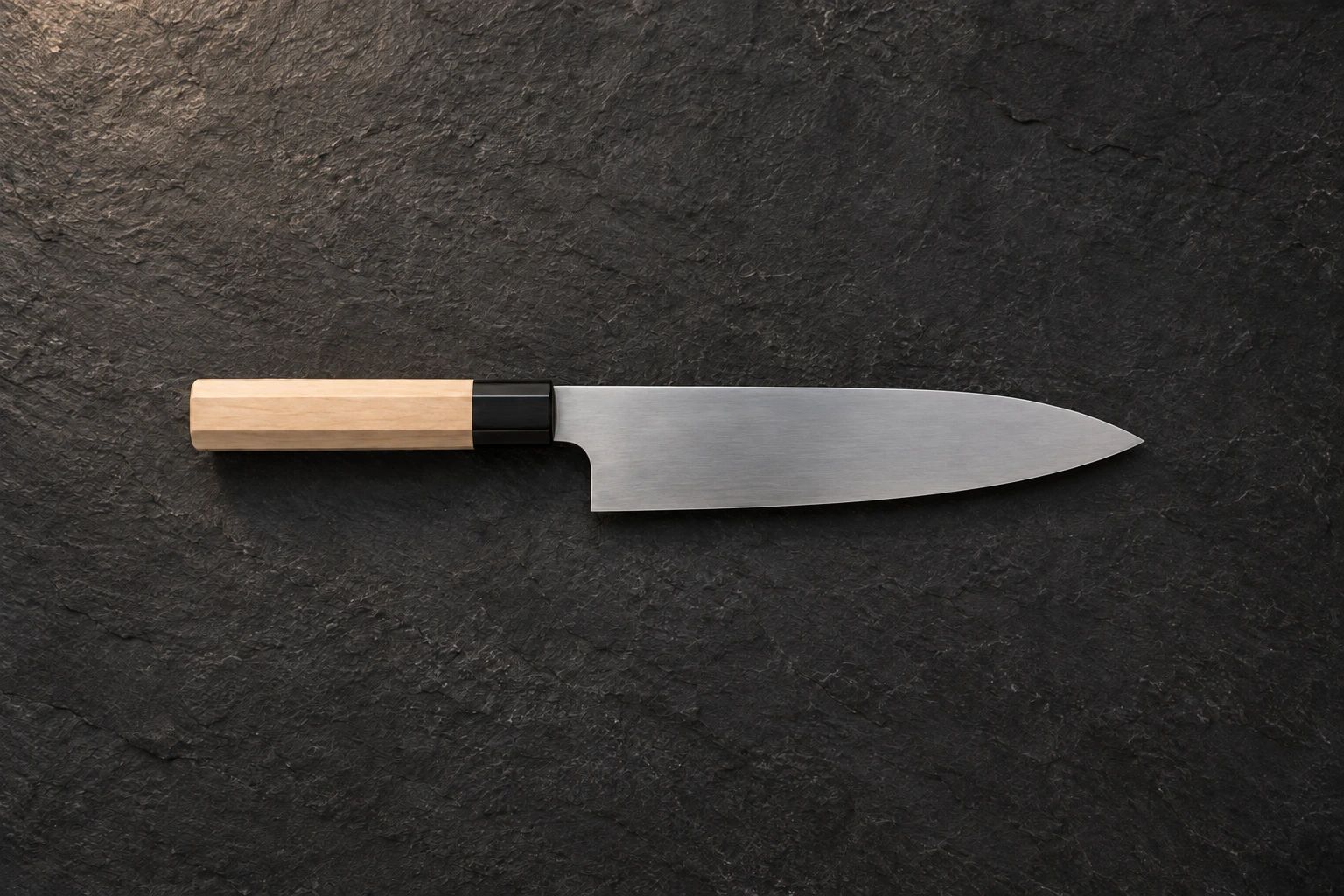 A gyuto with a wooden handle on dark slate, seen from above