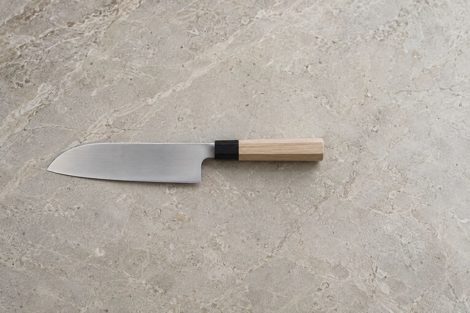 A single santoku with a pale wooden handle in the middle of a wide pale limestone surface