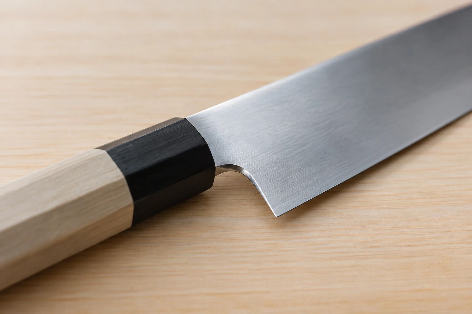 Close-up of where a gyuto's blade meets the black ferrule and octagonal wooden handle