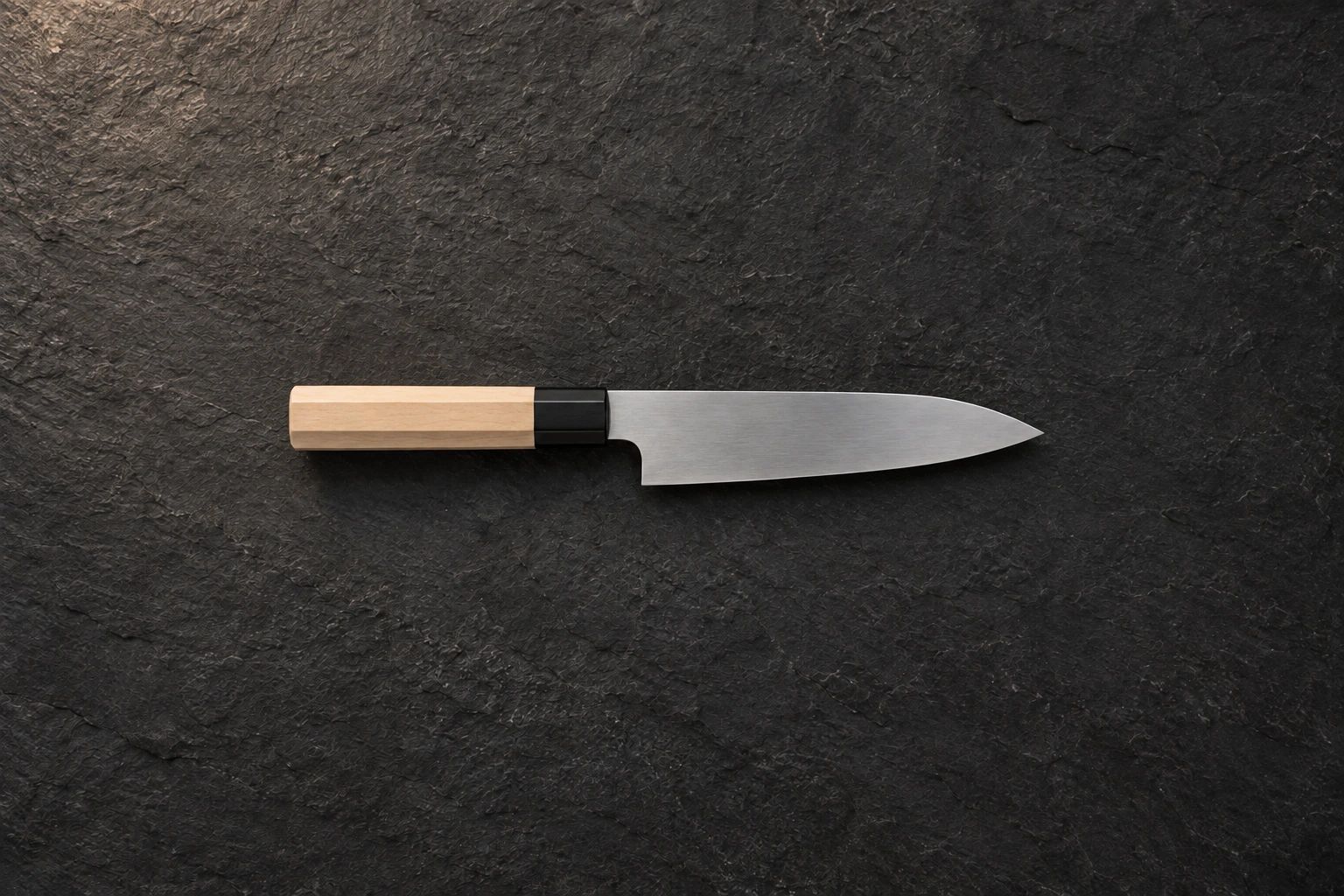 A small petty knife with a wooden handle on dark slate, seen from above