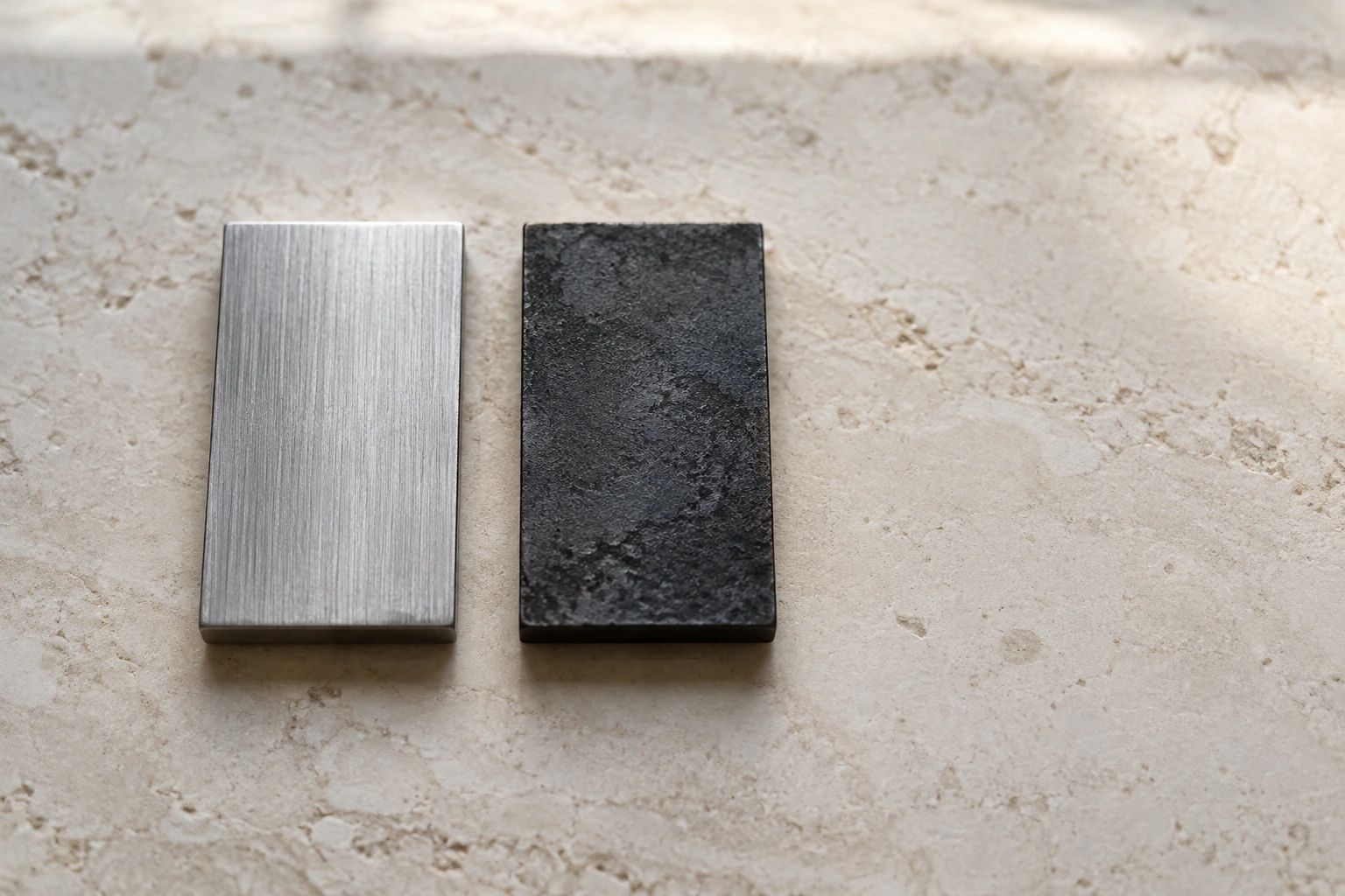 A brushed steel offcut and a black forge-scaled offcut of the same size side by side on limestone