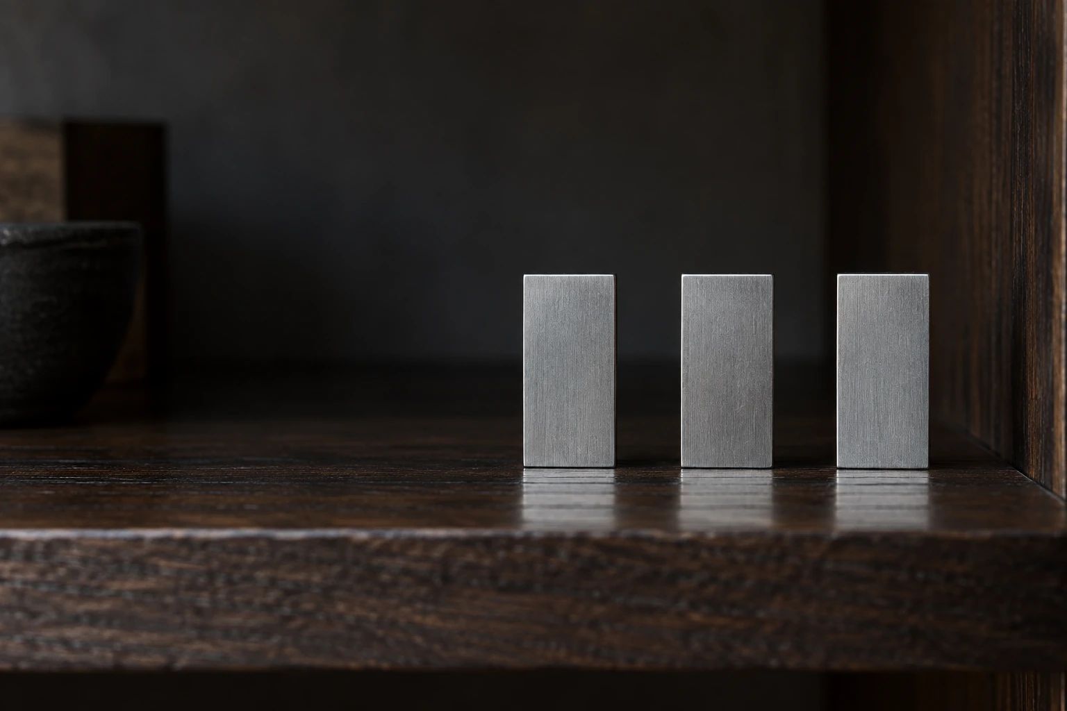 Three identical steel blocks standing evenly spaced on a dark oak shelf