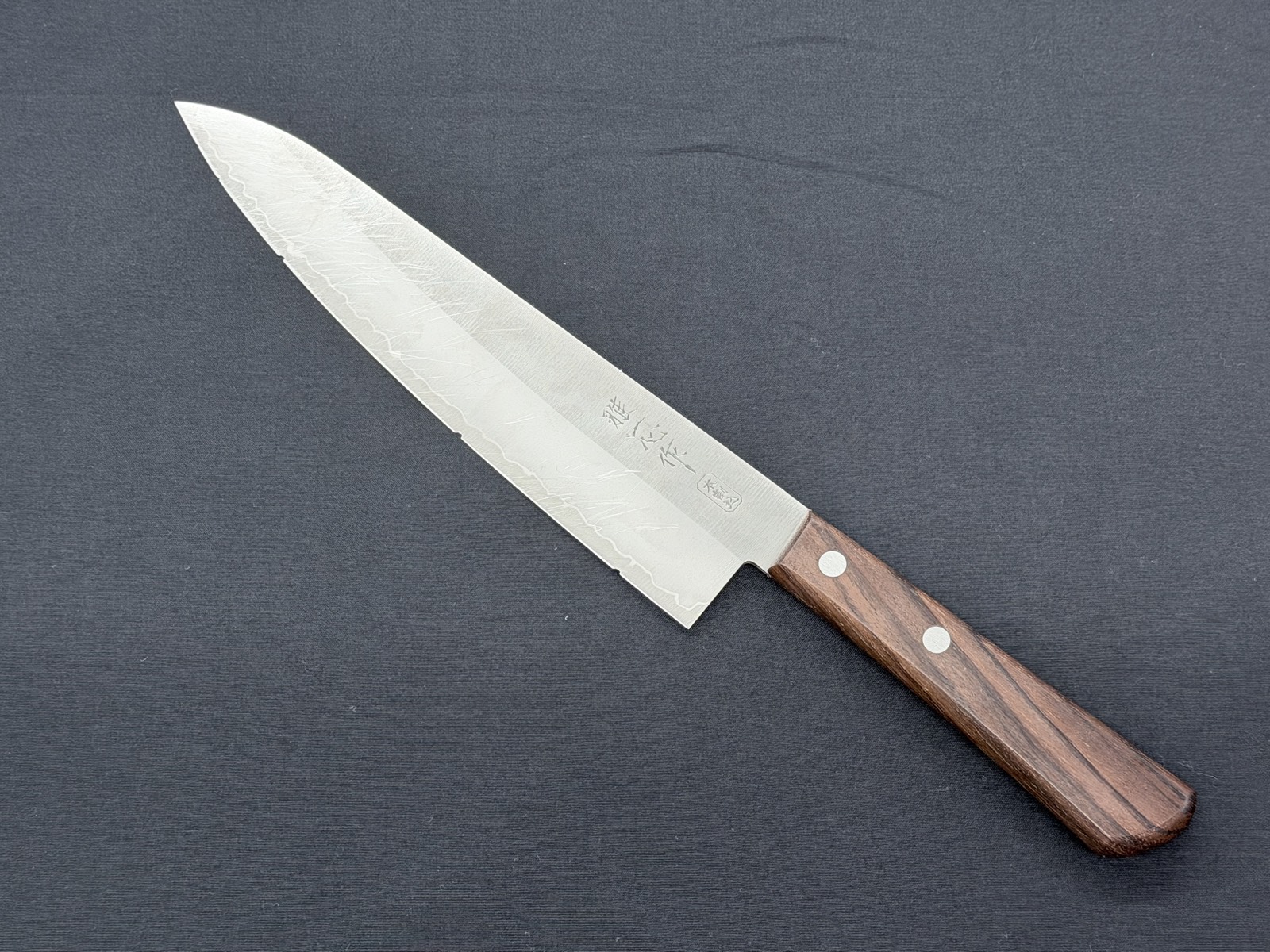 Sechs identische Santoku-Messer, an Klinge und Klingenflanke unter gleichen Bedingungen abgestumpft, vor der Abgabe zum Schärfen nebeneinander aufgereiht